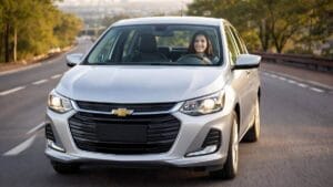 Mulher sorrindo dirigindo um Chevrolet Onix prata em uma estrada, imagem para banner da página inicial
