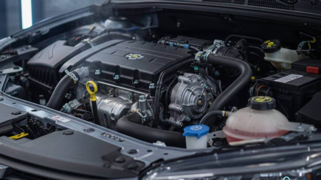 Vista detalhada do compartimento do motor de um Chevrolet Onix com o capô aberto, destacando o reservatório de expansão e mangueiras, com um ícone de temperatura e o texto 'Sistema de Arrefecimento Chevrolet Onix'.