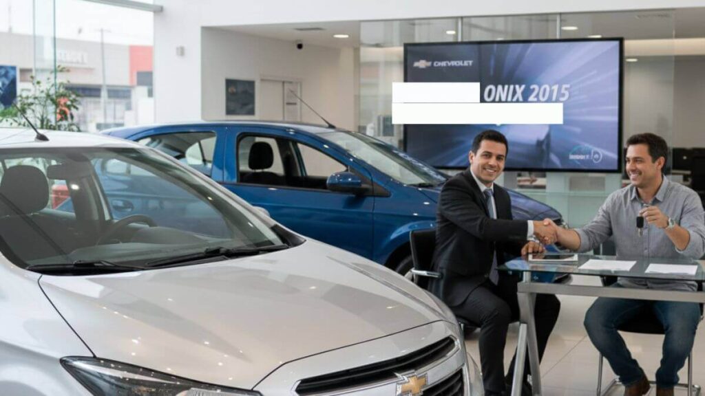 Interior de uma concessionária Chevrolet com dois modelos Onix 2015 em destaque (um prata em primeiro plano e um azul ao fundo). À direita, dois homens estão sentados à mesa; um vendedor de terno aperta a mão do cliente, que sorri segurando as chaves do carro novo.