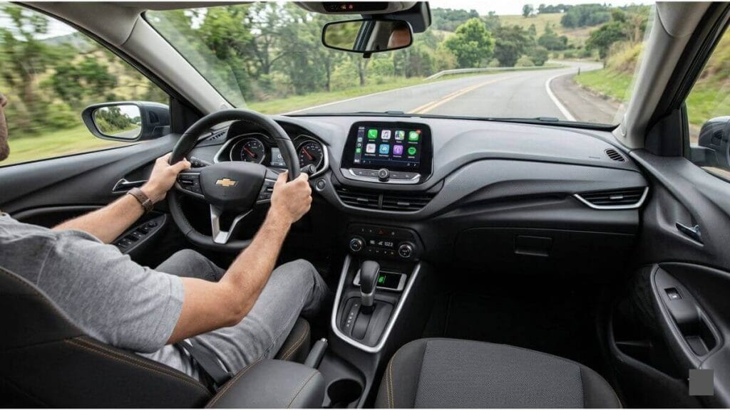 Vista de dentro do cockpit de um Chevrolet Onix Premier preto moderno, com o motorista segurando o volante em uma estrada sinuosa e cênica em Minas Gerais, Brasil, sob luz natural.