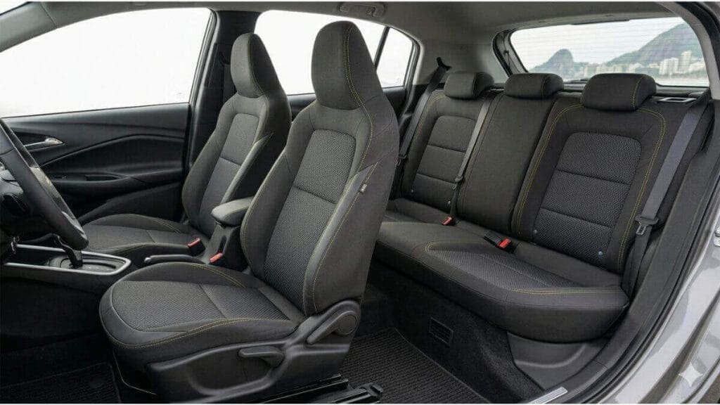 Visão interna lateral dos bancos dianteiros e traseiros de um Chevrolet Onix moderno, mostrando o design ergonômico e o acabamento em tecido premium escuro com costuras esportivas.