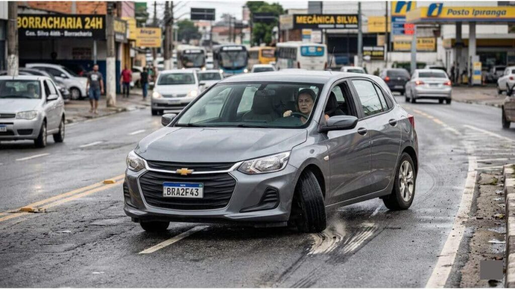 Chevrolet Onix cinza em uma rua urbana com a roda dianteira visivelmente torta e desalinhada, puxando para o lado e deixando rastro no asfalto.