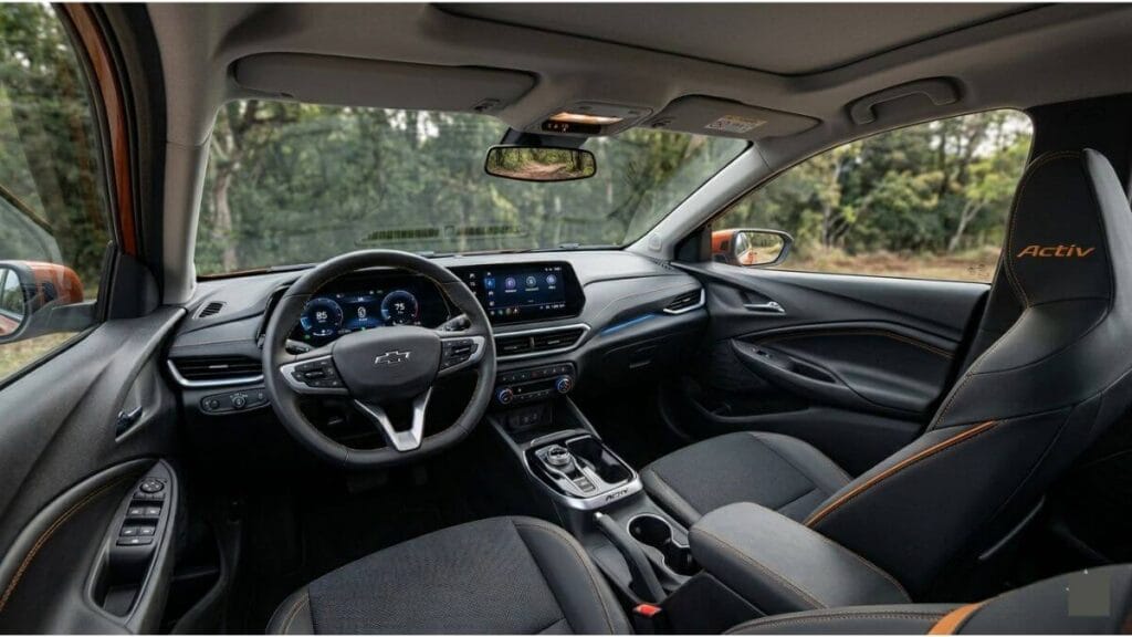 Interior do Novo Chevrolet Onix Activ 2027 Design interno do Chevrolet Onix Activ 2027 com acabamento premium escuro, costuras laranjas exclusivas da linha Activ, painel digital integrado e volante multifuncional.
