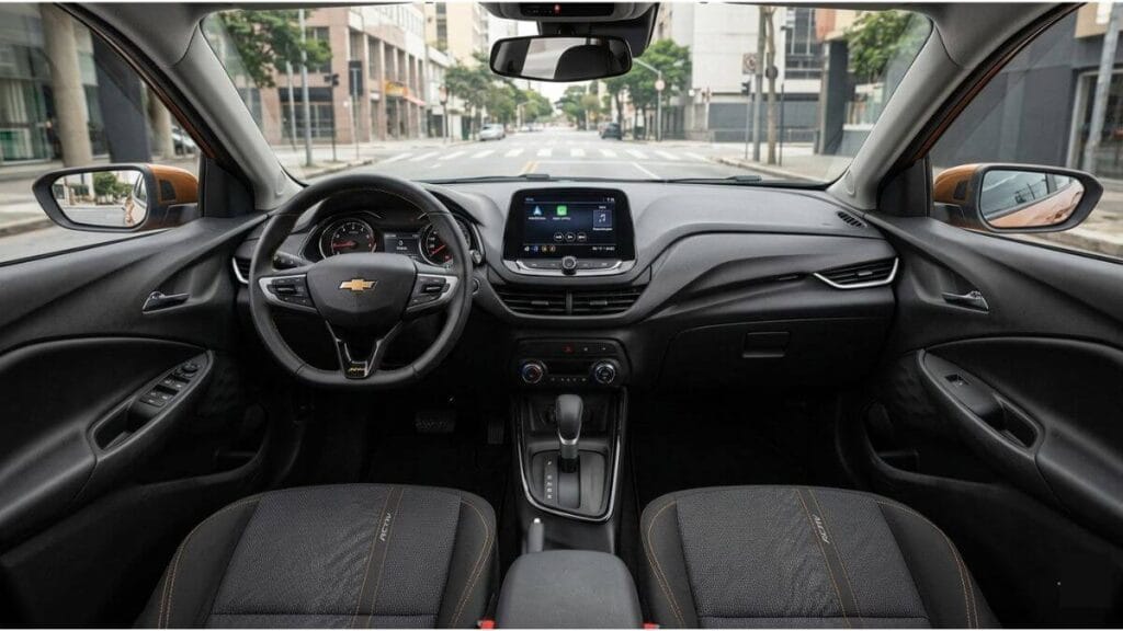 Interior Chevrolet Onix Activ Visão frontal do painel interno do Chevrolet Onix Activ, destacando o volante multifuncional, a central multimídia MyLink, o câmbio automático e o acabamento em tons de preto e laranja.